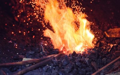 Anonymous farrier with tongs heating iron in hot furnace while working in blacksmith workshop